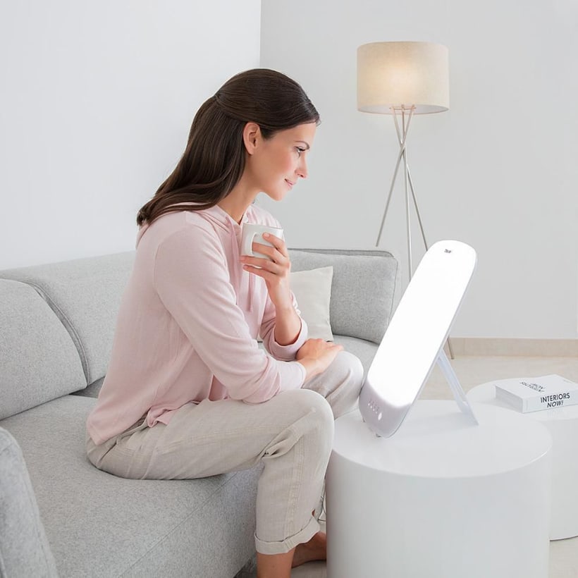 Femme utilisant la lampe de luminothérapie Beurer TL 85 dans son salon